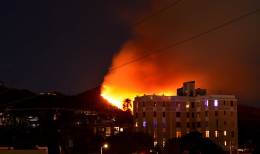 A large apartment building is at the right foreground, with a fire erupting on the hillside behind it. The photo is taken at night with a long exposure, making the fire very bright