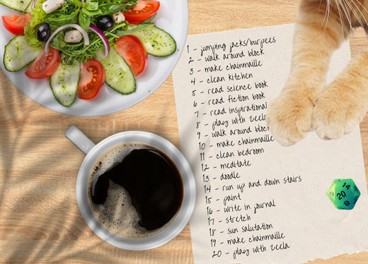 Aerial view of a morning breakfast table with a plate of veggies, a cup of coffee, a handwritten list, 2 cat paws and a green 20-sided die