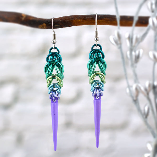 Chainmaille earrings with acrylic spike hanging from a branch. Earrings are in the colors to best match the neptunic pride flag - teal, light teal, seafoam, light blue, lavender with a lilac spike