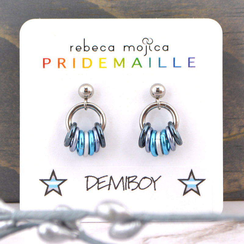 Demiboy earrings on a white card. These lgbtq pride stud earrings are made in colors to best match the demiboy flag - two shades of grey, white and light blue. Displayed on a card by artisan Rebeca Mojica