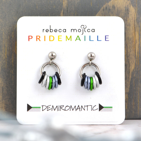 Small demiromantic pride chainmaille stud earrings on a white card. Each earring has a stainless steel ball with a steel link and 7 smaller links in the colors of the demiromantic pride flag - black, 2 grey, green, 2 white and black