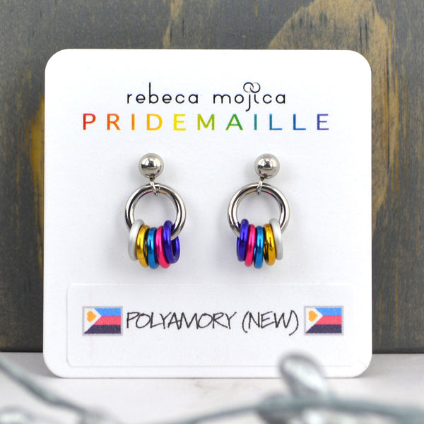 Tiny polyamorous pride chainmaille earrings on a card. Earrings are on a small stainless steel stud with a ball. Hanging from the ball is a steel link with 5 smaller links in the colors of the new polyamory tricolor pride flag by polyamproud - white, gold, blue, pink and purple. Card reads Rebeca Mojica PRIDEMAILLE Polyamory (new) and shows an image of the new flag