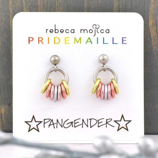 Tiny Pangender Pride chainmaille earrings displayed on a card. Earrings are on a post with a small steel ball. From the ball hangs a steel hoop that has 7 links hanging from it in the colors of the pangender pride flag: pastel yellow, peach, pink and white. The earring card reads Rebeca Mojica at top, the second line reads PRIDEMAILLE in rainbow color fonts. The bottom of the card has a sticker with the word PANGENDER flanked by 2 stars in the color of the pangender flag