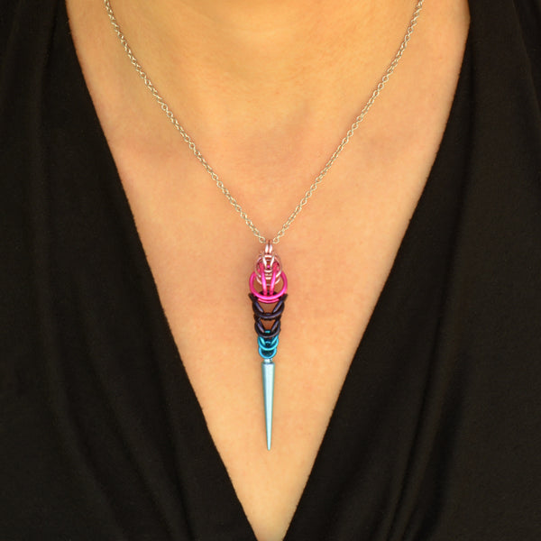 Omnisexual pride pendant being worn. Pendant is chainmaille in the colors of the omnisexual pride flag - light pink, hot pink, dark purple and blue, with a light blue acrylic spike at the bottom.