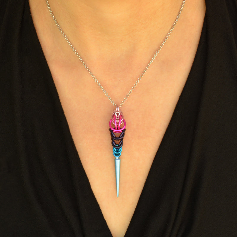 Omnisexual pride pendant being worn. Pendant is chainmaille in the colors of the omnisexual pride flag - light pink, hot pink, dark purple and blue, with a light blue acrylic spike at the bottom.