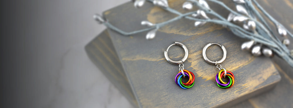 LGBTQ pride rainbow swirl chainmaille earrings on huggie hoops shown displayed on grey wood.